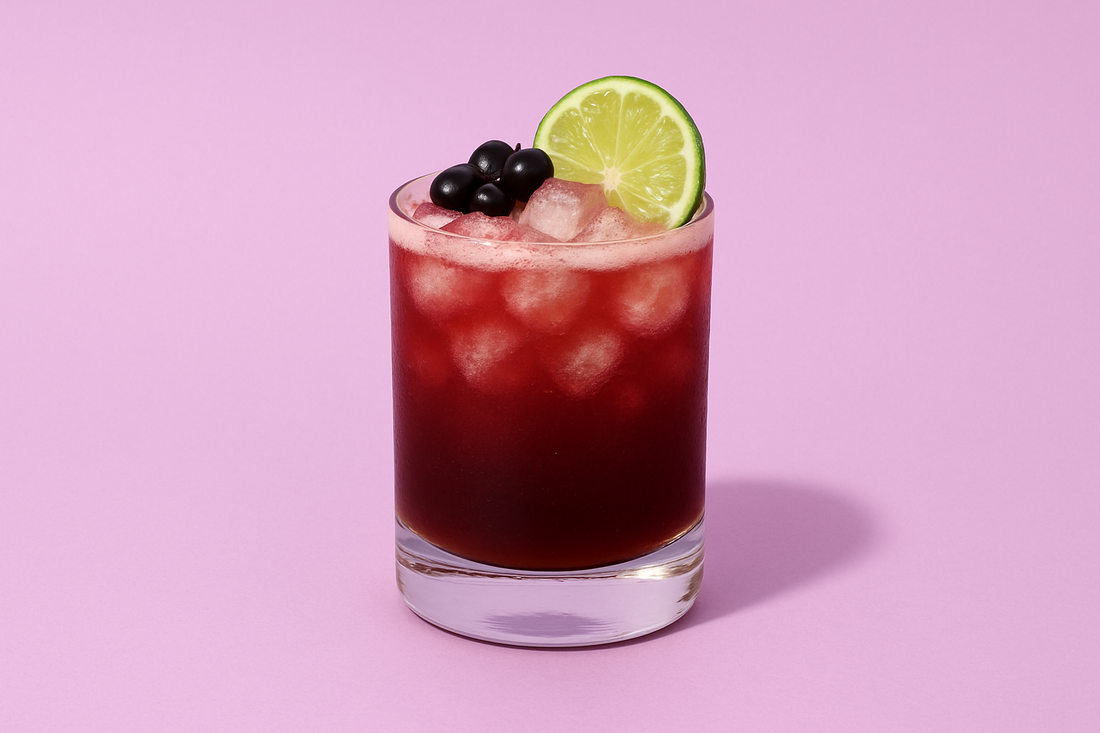 Vibrant cranberry mocktail in a clear glass filled with ice, garnished with a lime wheel and dark berries, set against a soft purple background. One of DASH Water's easy winter mocktail recipes.
